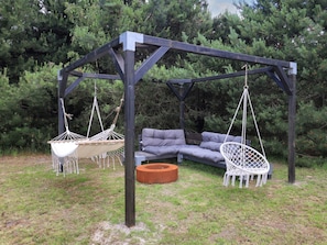 A wooden pergola with two white hanging chairs and a grey sofa. - 4 Star Holiday Home in Vaeggerlose (Vaeggerlose)