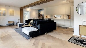 A modern living room with a black sofa, a small coffee table, and a dining area with white cabinets. - 4 Star Holiday Home in Vaeggerlose (Vaeggerlose)