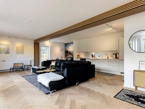 A modern living room with a black sofa, a small coffee table, and a dining area with white cabinets. - 4 Star Holiday Home in Vaeggerlose (Vaeggerlose)