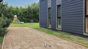 A playground with a slide and swings, a sand court with croquet balls, and a building with large windows.