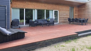 A modern outdoor deck with a wooden floor, a sofa set, and a dining table with chairs. - 4 Star Holiday Home in Vaeggerlose (Vaeggerlose)