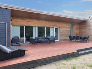 A modern outdoor deck with a wooden floor, a sofa set, and a dining table with chairs. - 4 Star Holiday Home in Vaeggerlose (Vaeggerlose)