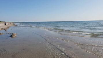 A beach with clear water and a person walking.