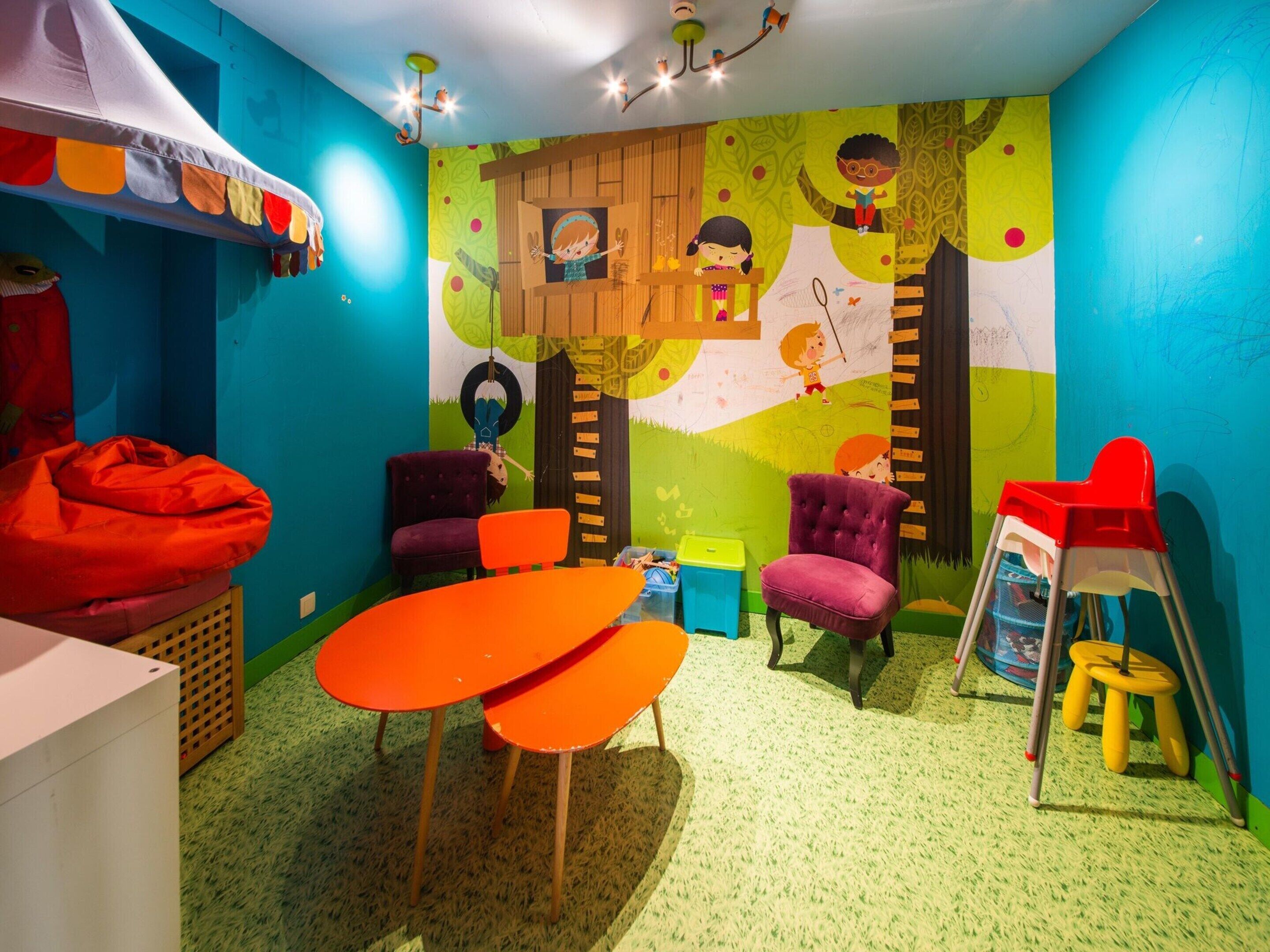 Ein farbenfroher Spielraum für Kinder mit einer großen Wandmalerei, einem roten Sitzsack und einem kleinen Tisch.