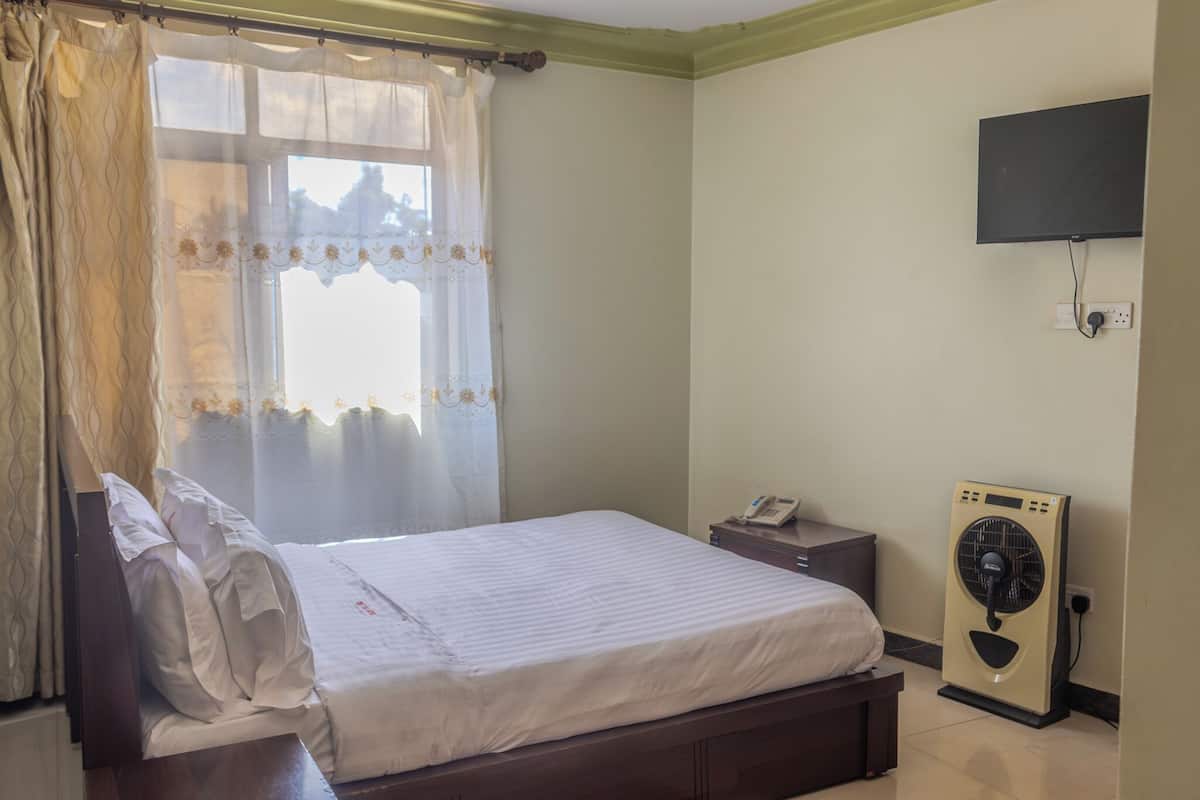 Un dormitorio con cama, mesita de noche, teléfono, televisor montado en la pared y ventilador de pie.