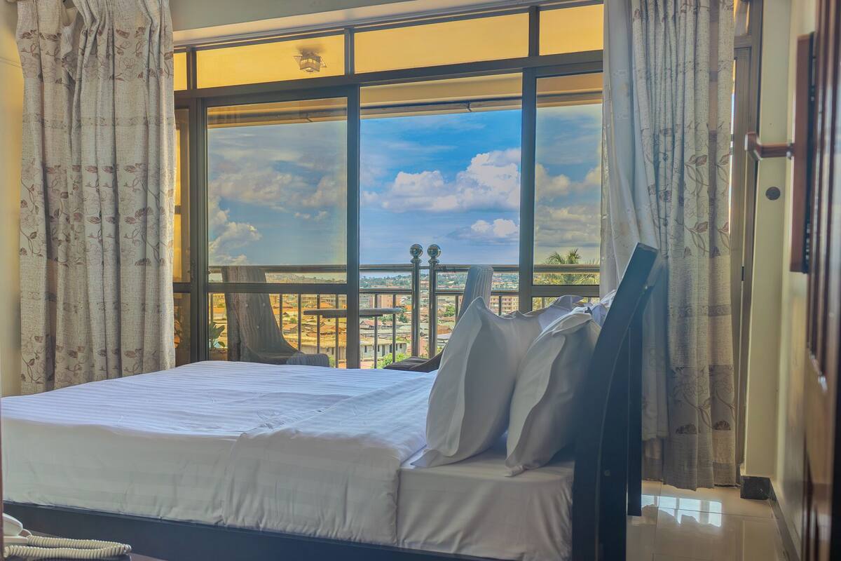 Una habitación de hotel con un ventanal grande, una cama, una mesita de noche y un teléfono.