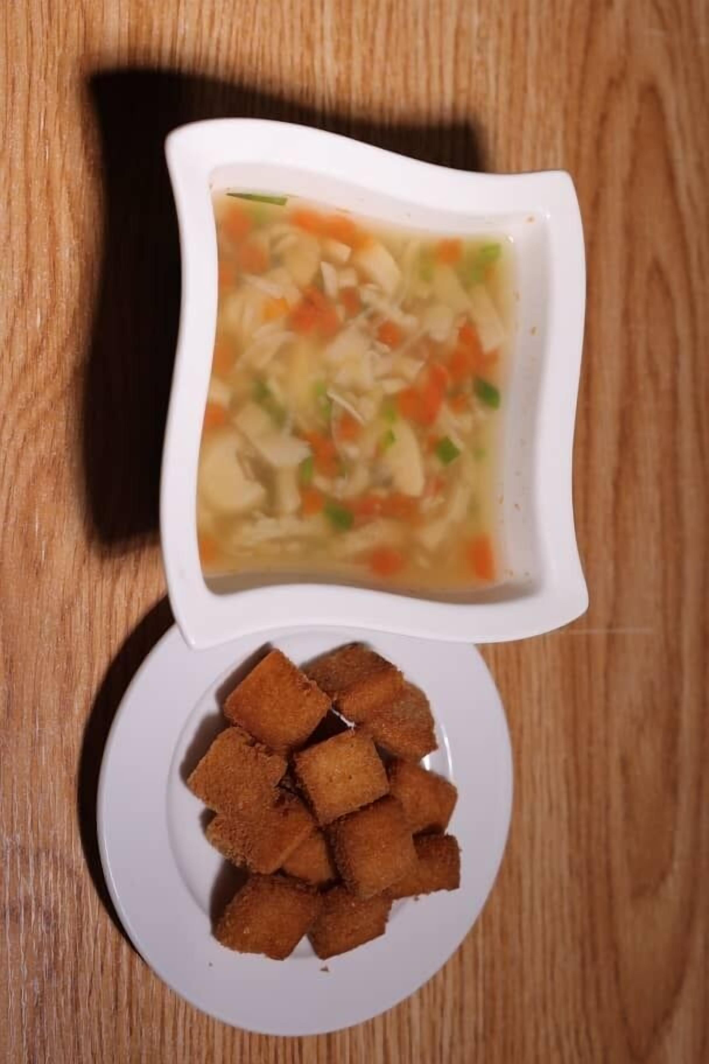 A white bowl of soup with vegetables and a plate of fried items.