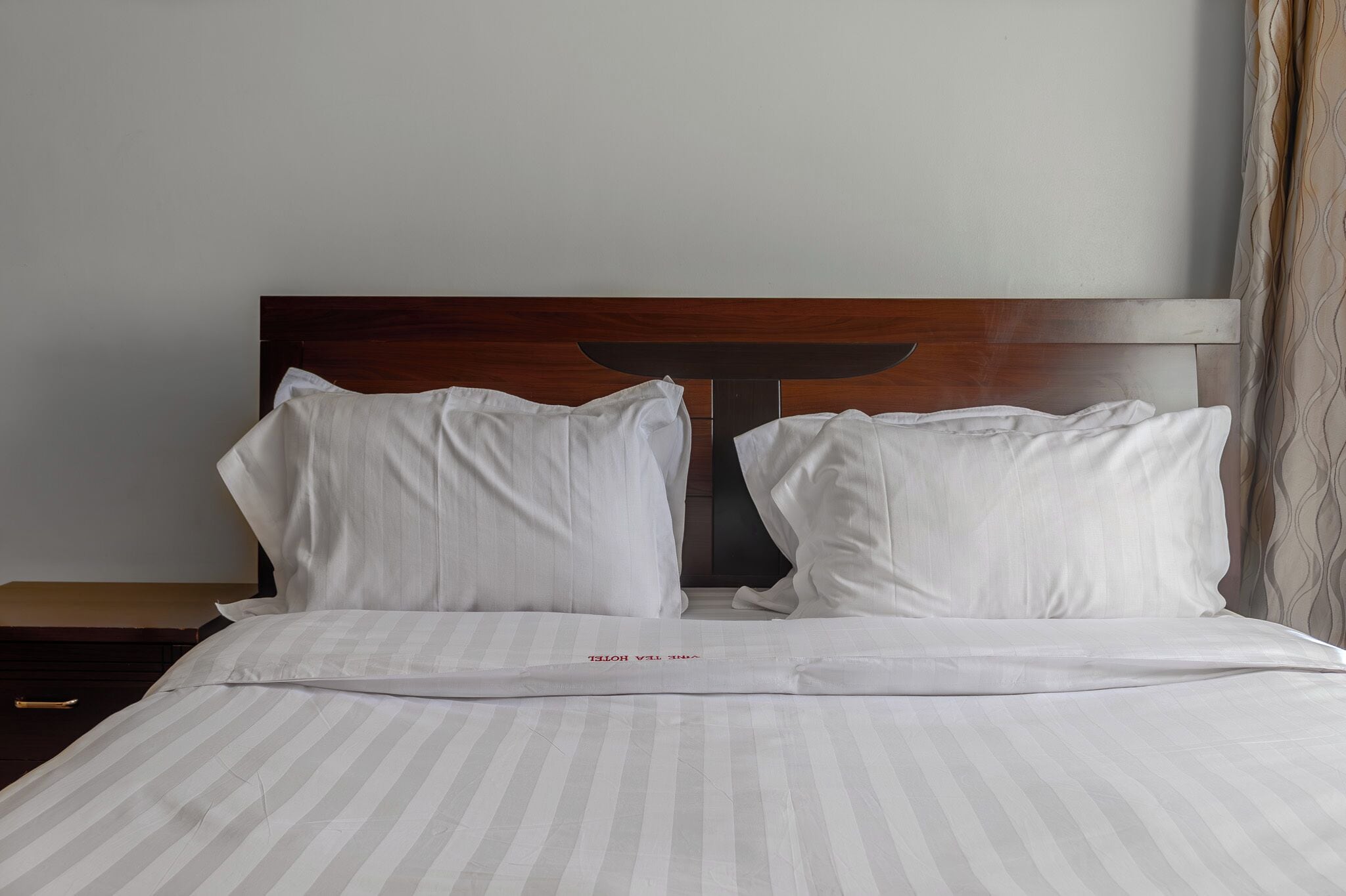 A neatly made bed with white pillows and a striped bedspread, a wooden headboard, and a bedside table with a lamp.