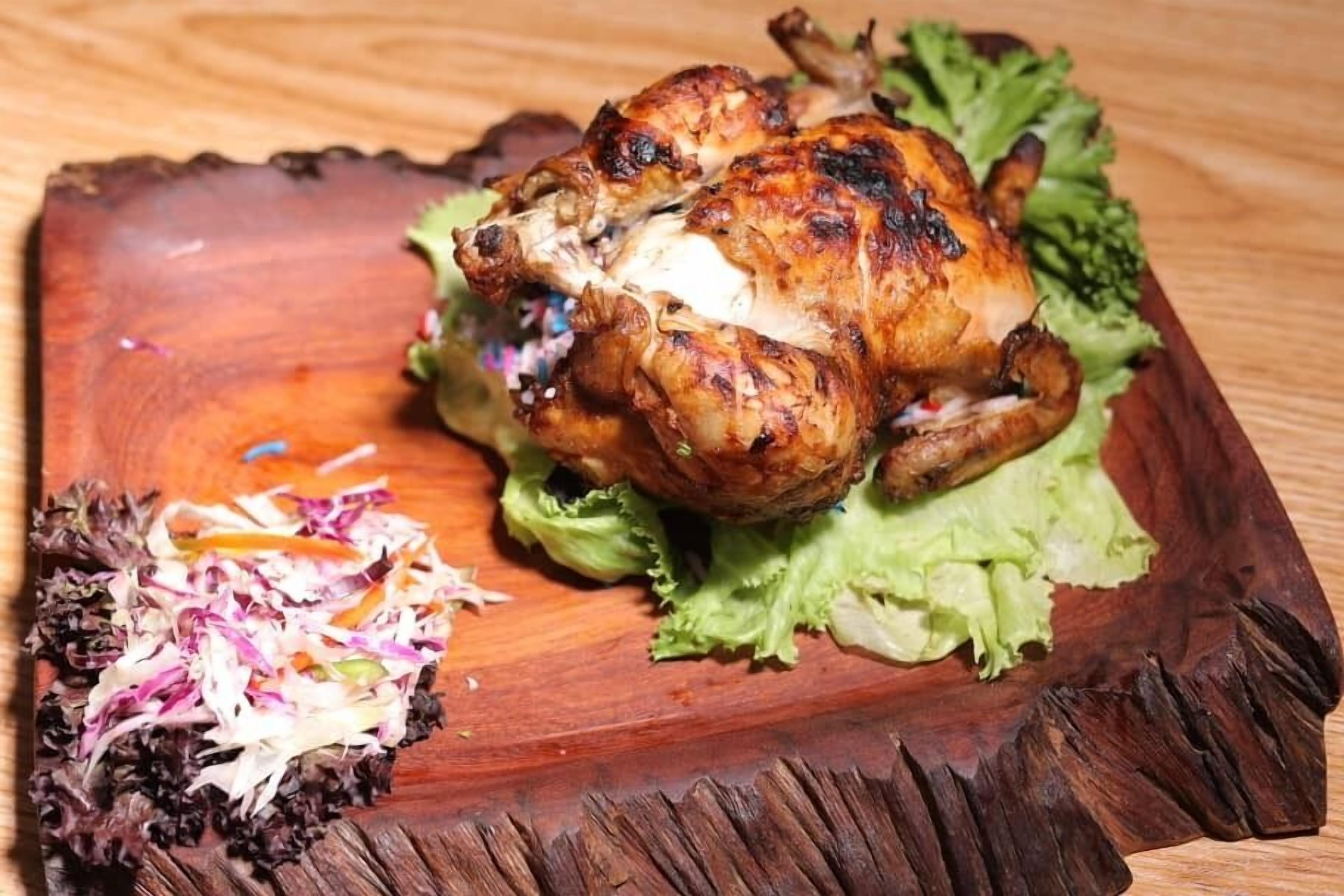 A roasted chicken on a wooden board with lettuce and a side salad.