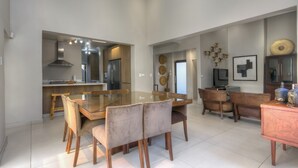 Ein geräumiger Essbereich mit Glastisch und Holzstühlen, eine Küche mit modernen Geräten sowie ein Wohnbereich mit Sofa und Dekoelementen.