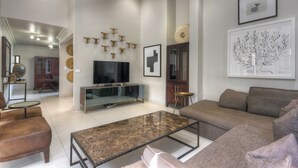 Ein modernes Wohnzimmer mit einem Flachbildfernseher, einem Marmortisch und einem braunen Sofa.