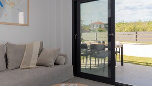 A modern living room with a sofa, a glass door leading to an outdoor patio, and a framed abstract painting on the wall. - SithoniaRS Ground Floor Gem in Nikiti (Nikiti)