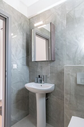 A bathroom with a pedestal sink, a mirror above it, and grey marble walls. - SithoniaRS Ground Floor Gem in Nikiti (Nikiti)