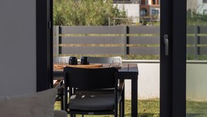 An outdoor dining area with a table, chairs, and a view of houses through a fence. - SithoniaRS Ground Floor Gem in Nikiti (Nikiti)