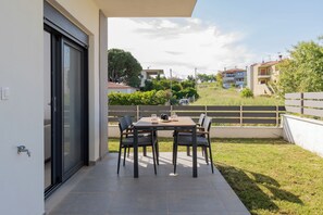 An outdoor patio with a table and chairs, a sliding glass door, and a view of neighboring buildings and greenery. - SithoniaRS Ground Floor Gem in Nikiti (Nikiti)