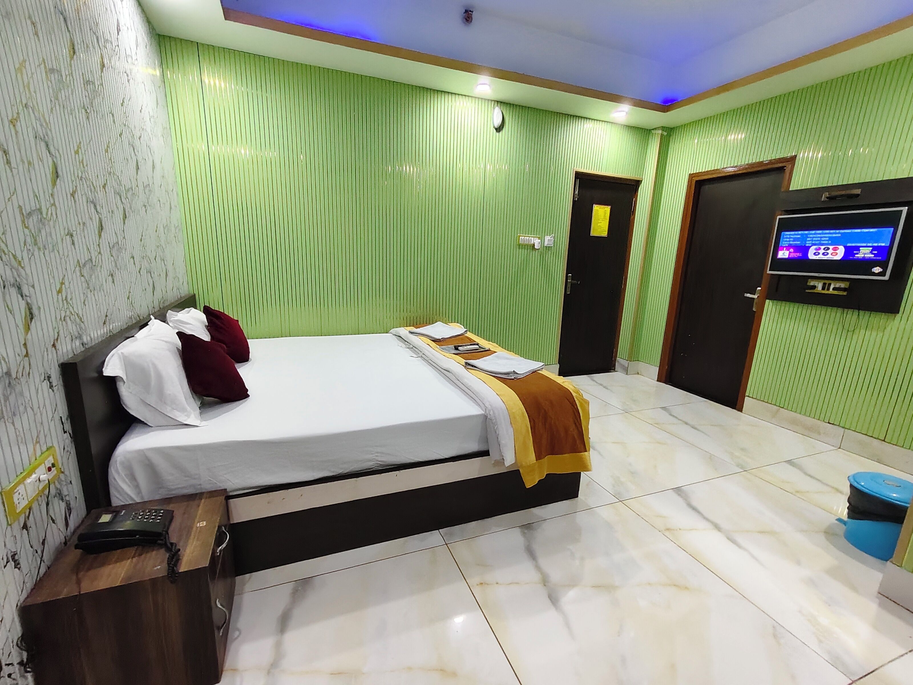 A hotel room with a bed, a desk with a telephone, a television mounted on the wall, and a door with a sign.