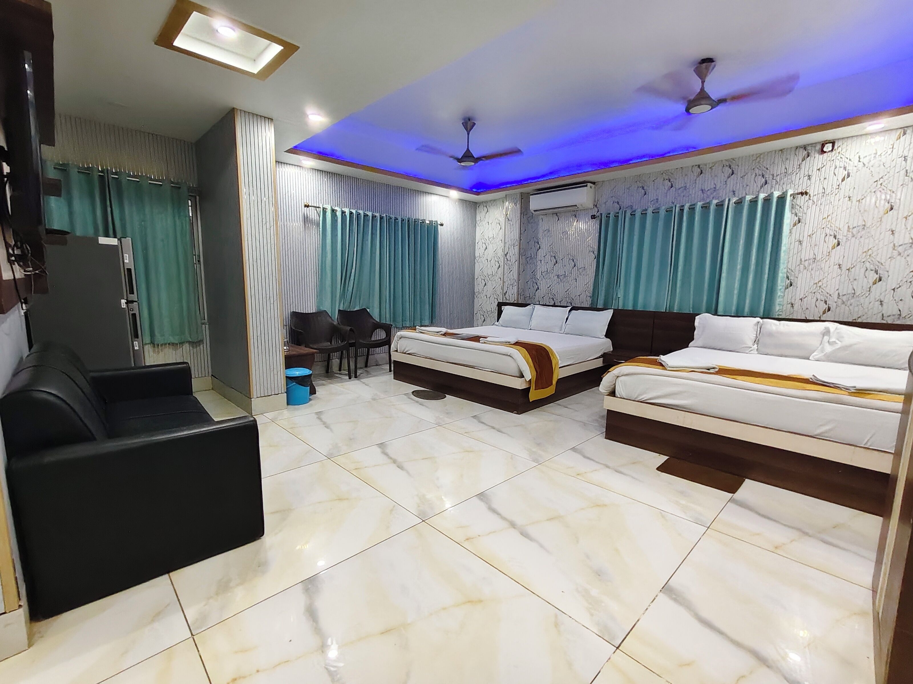 A hotel room with two beds, a desk, chairs, a TV, and an air conditioning unit.