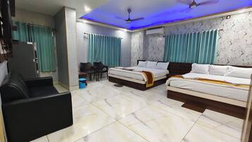 A hotel room with two beds, a desk, chairs, a TV, and an air conditioning unit.
