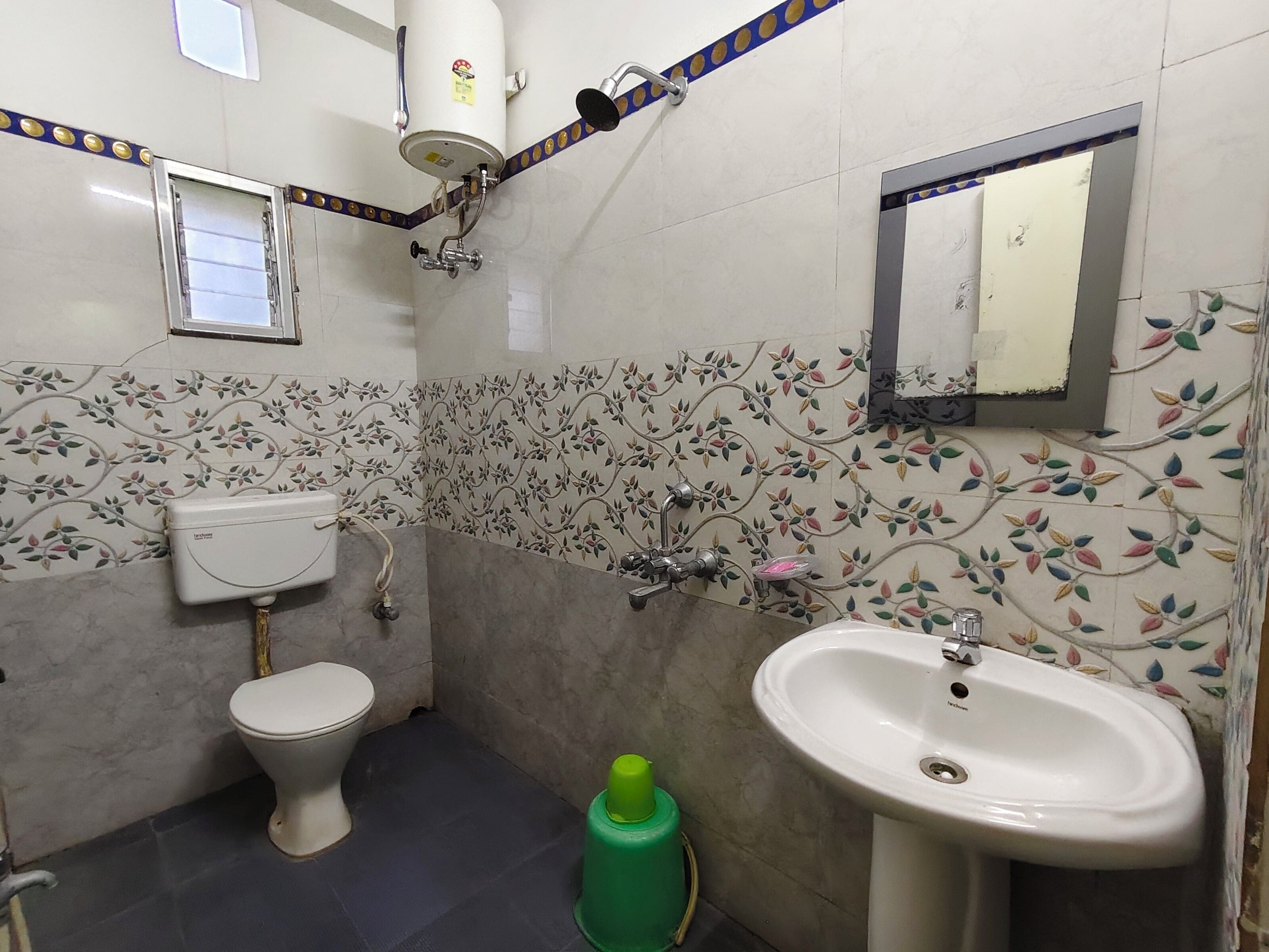 Et badeværelse med toilet, vask, brusebad og dekorative vægfliser.