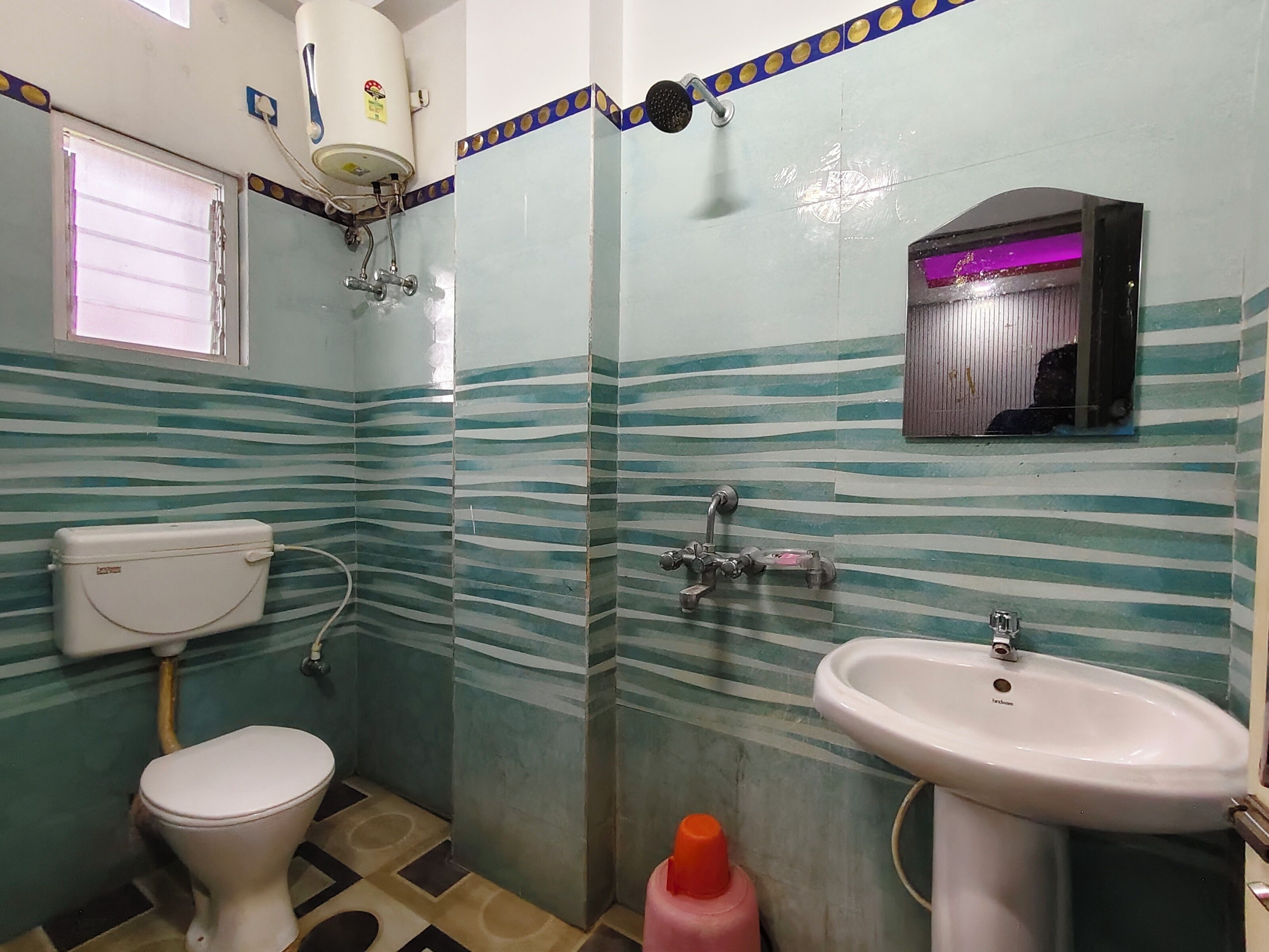 A bathroom with a toilet, sink, shower, and a window.