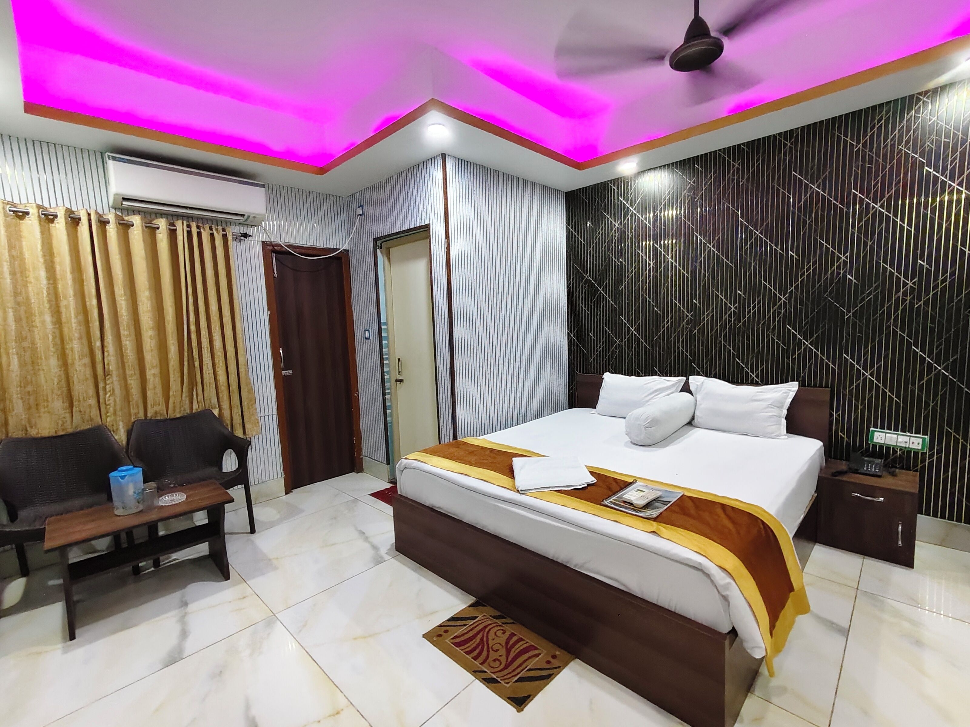 Una habitación de hotel con cama, mesita de noche, cortinas, ventilador de techo y pared con estampado.