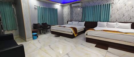 A hotel room with two beds, a desk, chairs, a ceiling fan, and an air conditioning unit.