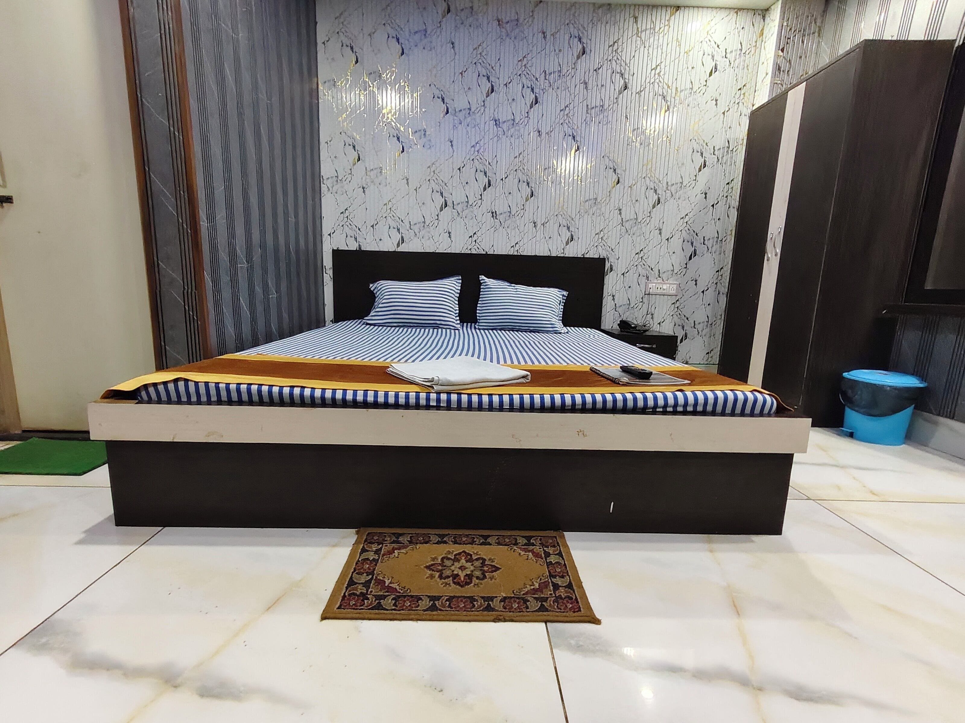 Un lit bien fait, avec une literie à rayures, une table de chevet avec une lampe et un tapis à motifs sur un sol carrelé.