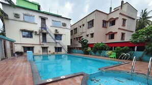 A swimming pool with a tiled deck, surrounded by buildings with multiple windows and balconies. - ICONIC Hotel Digha (Kanthi)