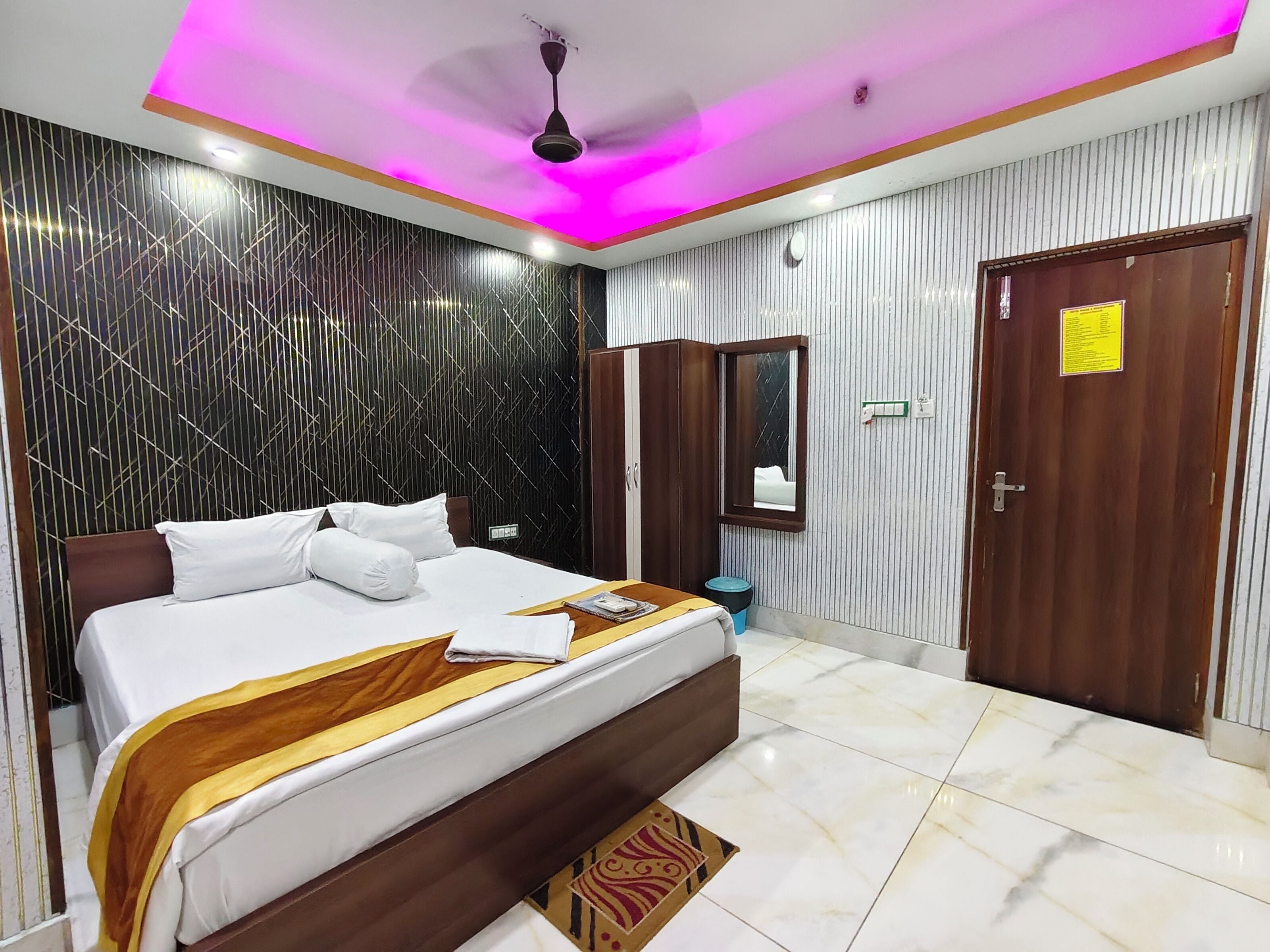 Una habitación de hotel con cama, ventilador de techo, espejo y puerta.