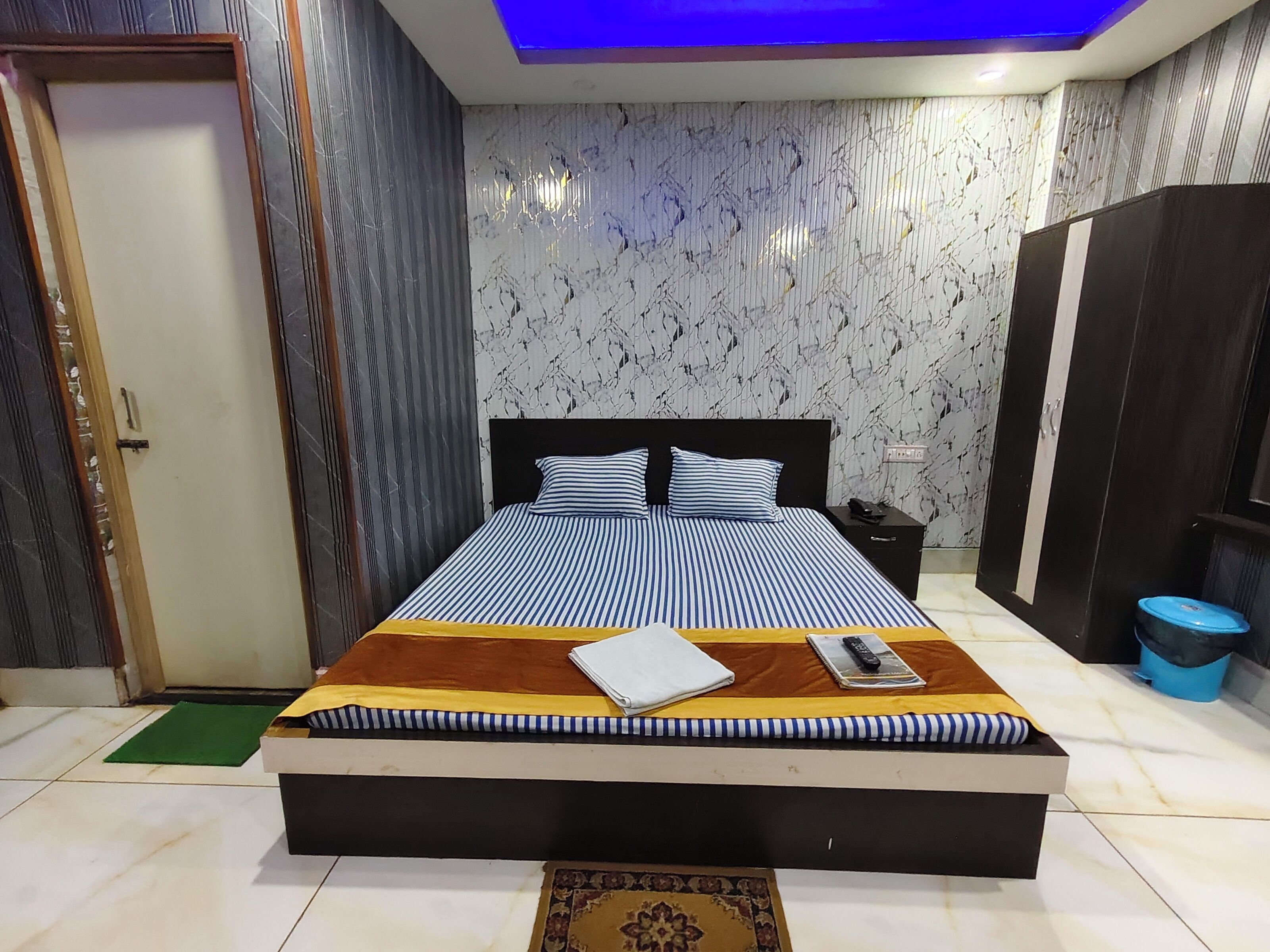 A bedroom with a bed, a nightstand, a wardrobe, and a blue trash bin.