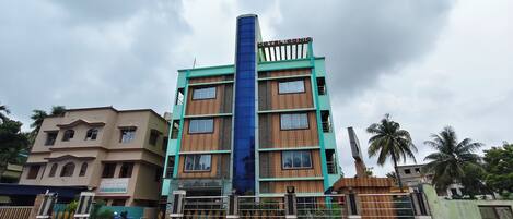 Un hôtel à plusieurs étages, reconnaissable à sa large bande bleue verticale, doté d’une entrée sécurisée par un portail et entouré d’une clôture.