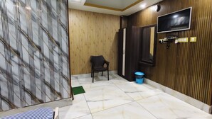 A room with a TV mounted on the wall, a black chair, a wardrobe, and a tiled floor. - ICONIC Hotel Digha (Kanthi)