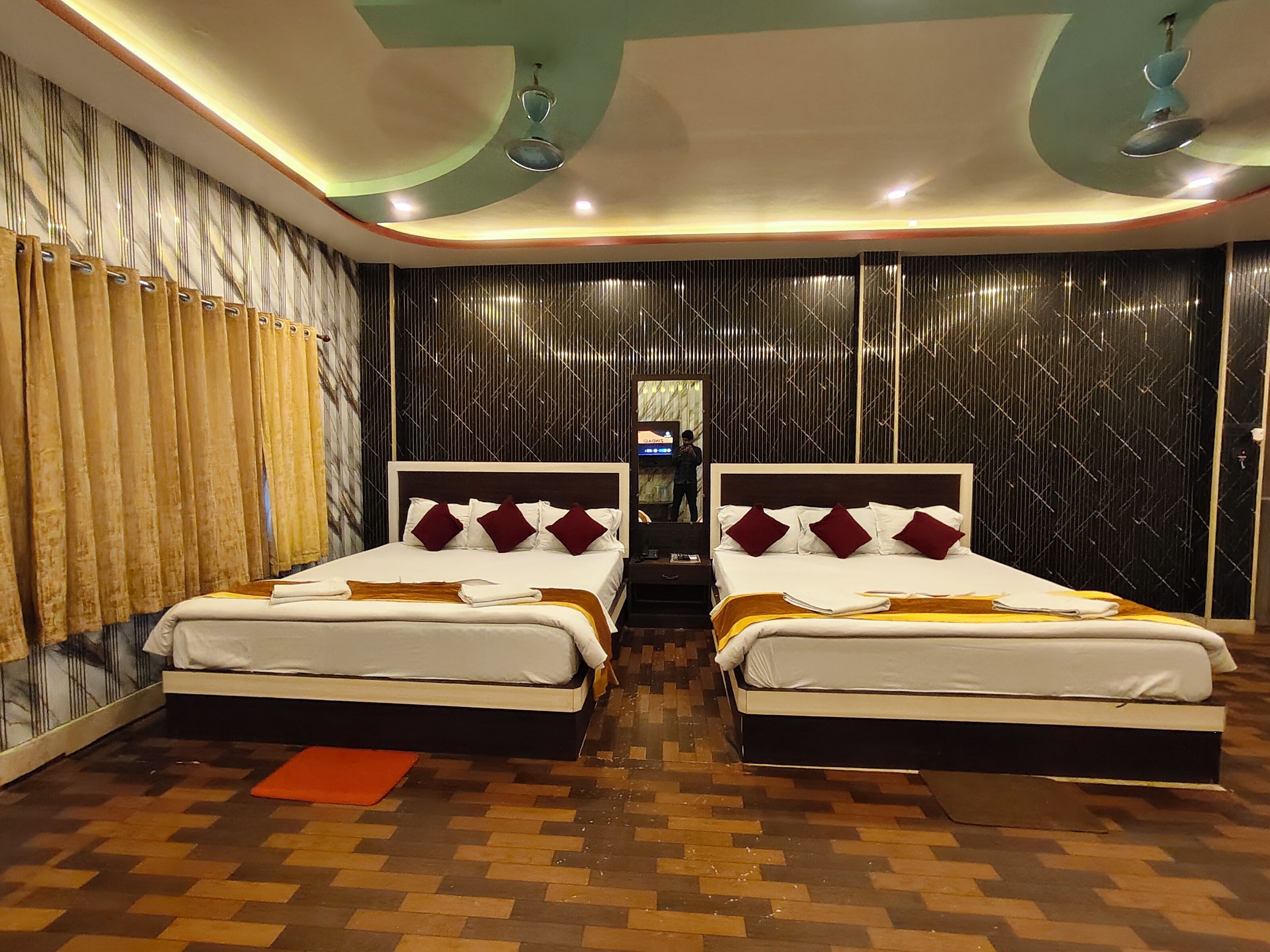 A hotel room with two beds, a mirror, a television, and a patterned wall.