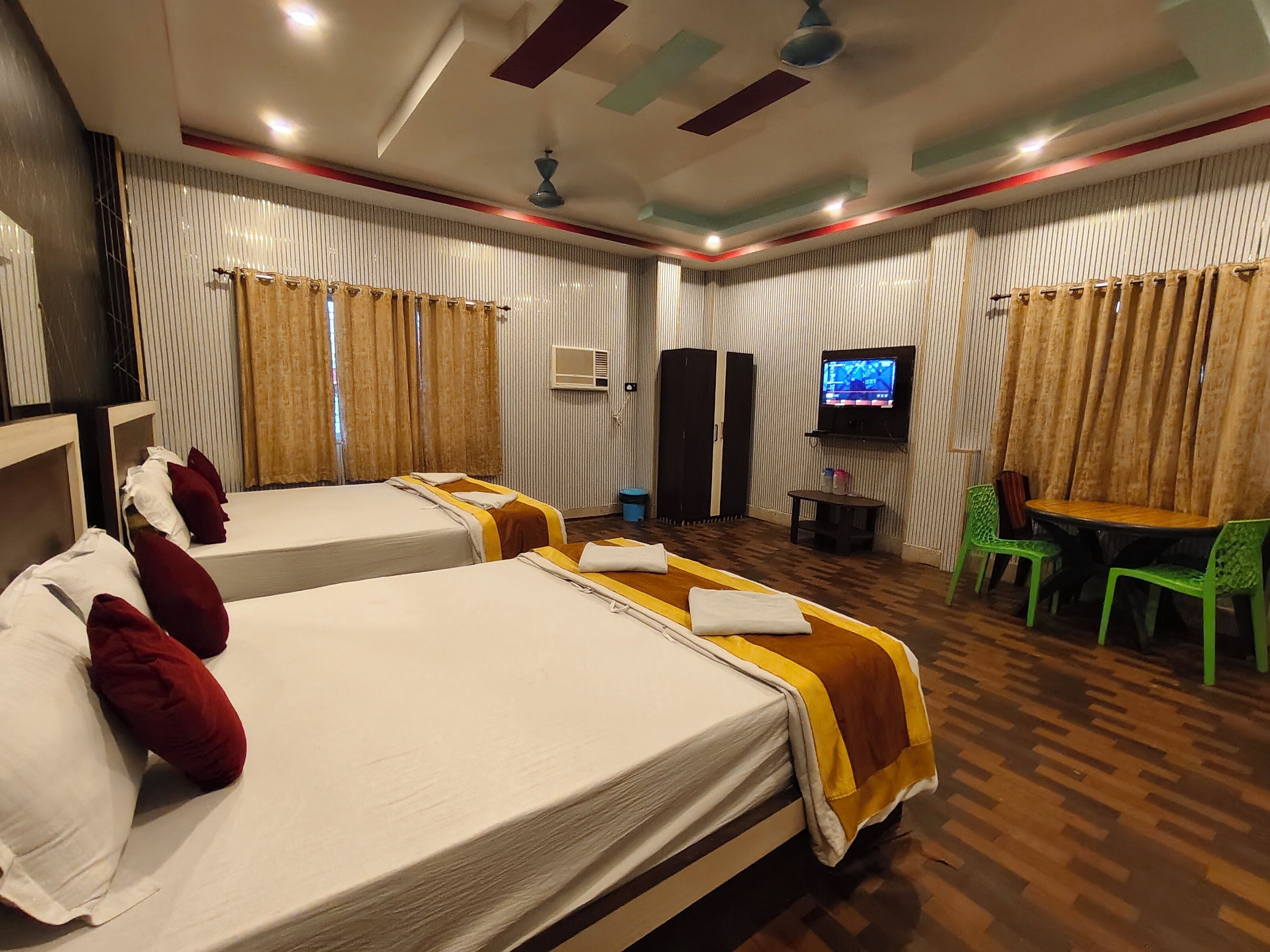 Habitación de hotel con dos camas, televisión, una mesita y una silla verde.