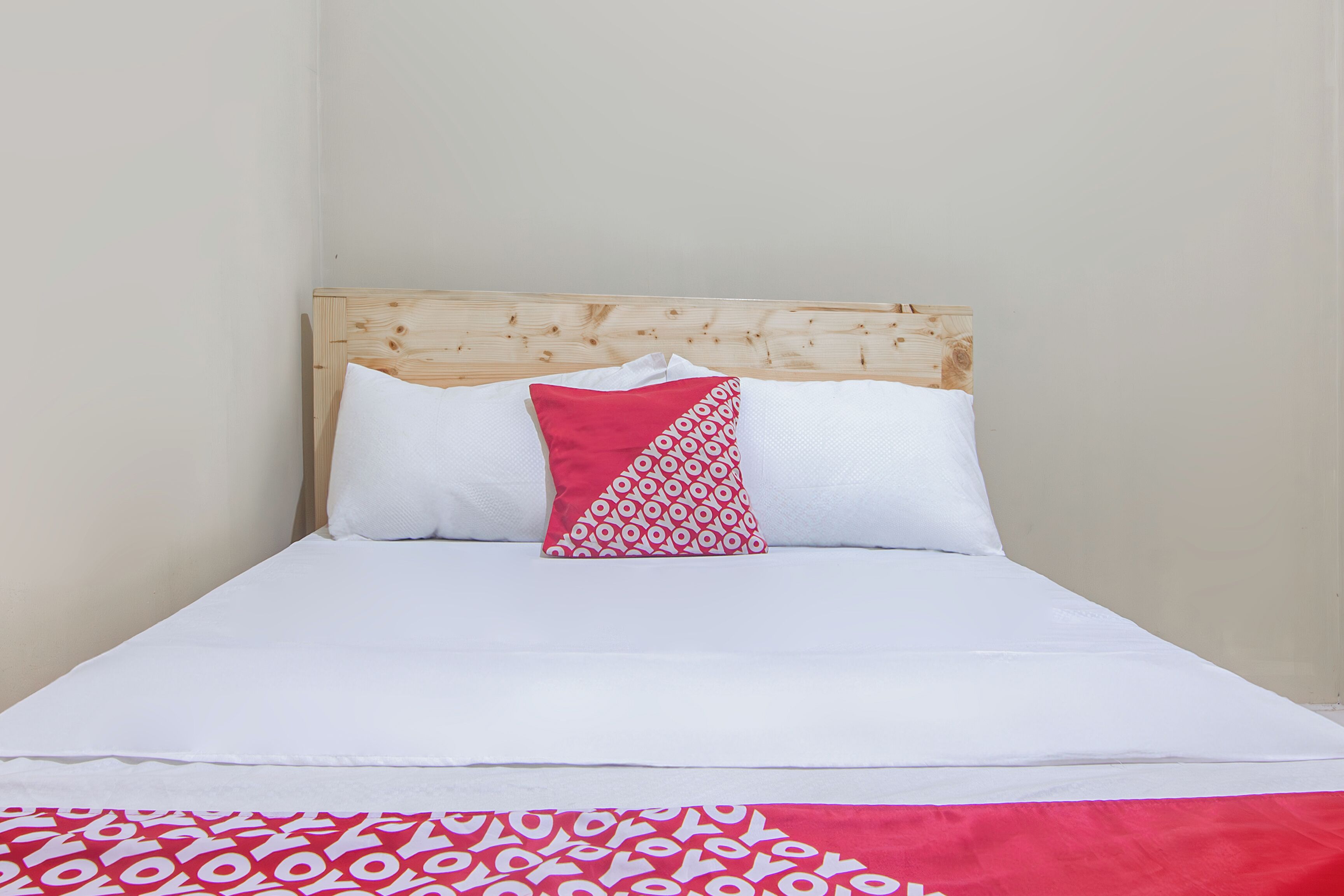 Ein Bett mit Holz-Kopfschild, weißer Bettwäsche und einem roten und weißen Kissen mit Muster.