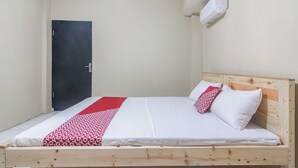 Una cama individual con estructura de madera, ropa de cama blanca y una manta estampada en rojo y blanco.