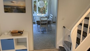 A hallway leading to a dining area with a table and chairs, a white staircase, and a painting on the wall. - Shell Modern Retreat (Dornum)