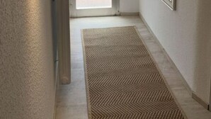 A narrow hallway with a radiator, a patterned rug, a door leading outside, and a mirror on the wall. - Shell Modern Retreat (Dornum)