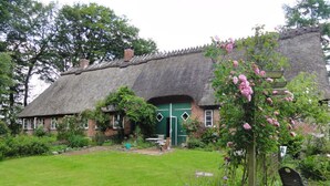 A thatched-roof cottage with a green door, surrounded by a well-maintained garden with flowering plants and a lawn. - Romantic Thatched Roof House (Schnarup-Thumby)