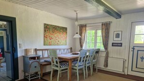 A dining area with a wooden table and chairs, a bench, a painting on the wall, and a window with curtains. - Romantic Thatched Roof House (Schnarup-Thumby)