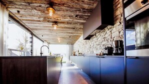 A modern kitchen with a stone wall, wooden ceiling, and a long countertop. - Maison Heurelijk Modern Finished Near Somme-leuze (Somme-Leuze)