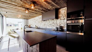 A modern kitchen with a stone backsplash, a large island, and built-in appliances. - Maison Heurelijk Modern Finished Near Somme-leuze (Somme-Leuze)