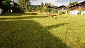 A grassy outdoor area with a seesaw, wooden buildings, and a large tree. - Holiday Apartment Brandl Haus 92 (Arrach)