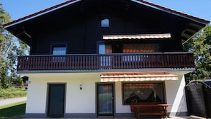 A two-story chalet with a balcony, a covered outdoor seating area, and a large sliding glass door. - Holiday Apartment Brandl Haus 92 (Arrach)