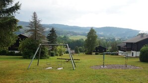 A grassy outdoor area with a swing set, a small climbing structure, and a fenced play area. - Holiday Apartment Brandl Haus 92 (Arrach)