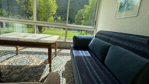 A living room with a large window, a sofa, a table, and a patterned rug. - Beautiful Apartment in Gortipohl With Garden (Sankt Gallenkirch)