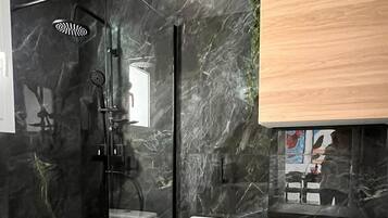 A modern bathroom with a glass-enclosed shower, a toilet, and a washing machine.