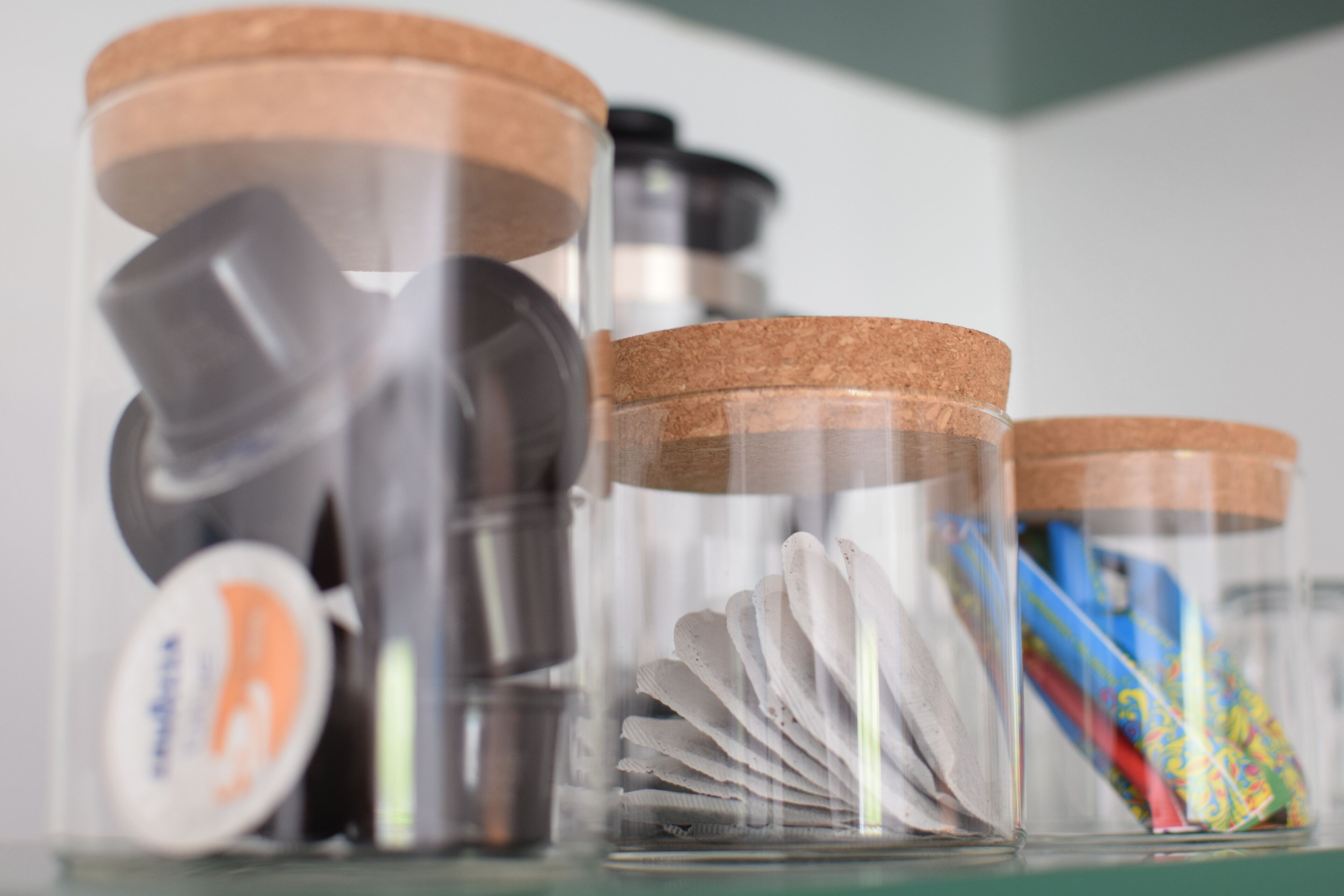 Una estantería con varios recipientes, incluyendo frascos con tapones de corcho y un recipiente transparente con objetos blancos.