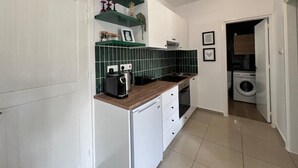 A compact kitchen with white cabinets, a wooden countertop, and a built-in washing machine in the adjacent room.
