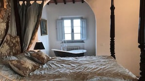 Een slaapkamer met een hemelbed, een raam en een inbouwbad.